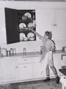 Image of Daughter of Mormon farmer putting away dishes in kitchen cabinet. Box Elder County, Utah